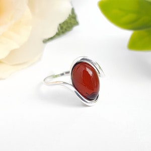 May include: A silver ring with a red oval-shaped gemstone set in a curved band.