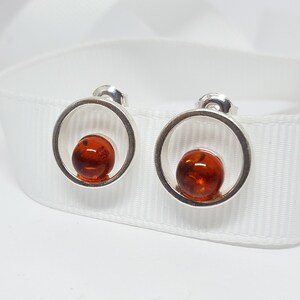 May include: A pair of silver earrings with a round amber stone in each. The earrings are simple and elegant.