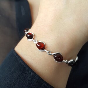 May include: A silver bracelet with red oval-shaped stones. The bracelet has a delicate, twisted design.