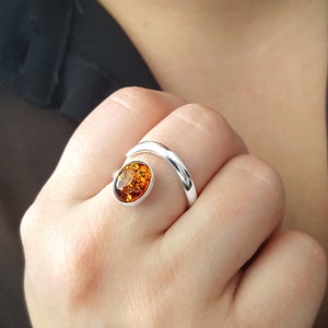 Peut inclure: Une bague en argent avec une grande pierre ovale en ambre. La bande de la bague est une fine bande en argent incurvée qui s'enroule autour du doigt.