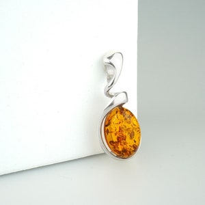 May include: A silver pendant with a swirl design and a round amber stone.