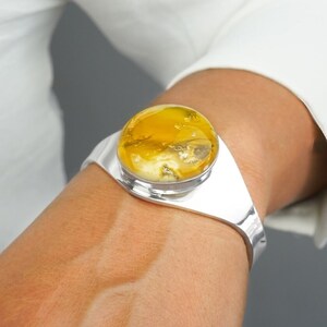 May include: A silver bangle bracelet with a large, round, yellow amber stone set in the centre.