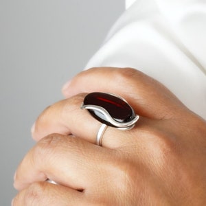 Puede incluir: Un anillo de plata con una piedra ovalada de color rojo oscuro engastada en un diseño ondulado.