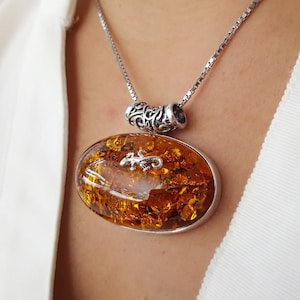 May include: A silver chain necklace with a large oval amber pendant featuring a silver lizard design. The pendant is set in a silver bezel.