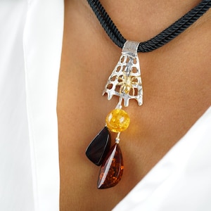 May include: A silver and gold pendant necklace with a honeycomb design and three amber stones. The necklace is on a black cord.