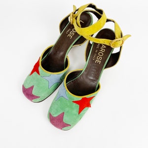 May include: A pair of green suede heeled shoes with a yellow ankle strap and a star pattern. The shoes are made in Italy by the brand "La Rose".
