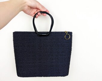 May include: A black beaded handbag with a black top handle and a gold ring zipper pull.