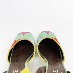 May include: A pair of yellow, green, blue, and red suede heeled sandals with a brown leather insole. The sandals have a star-shaped design on the top and the brand name "ROSE IN ITALY" is printed on the strap.