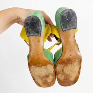May include: A pair of green and yellow suede heeled sandals with ankle straps. The sandals have a chunky heel and a square toe.
