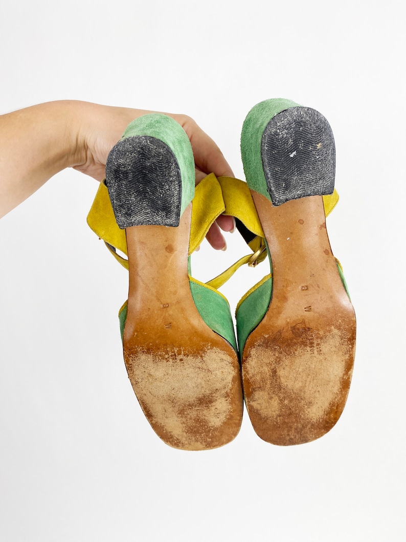 May include: A pair of green and yellow suede heeled sandals with ankle straps. The sandals have a chunky heel and a square toe.