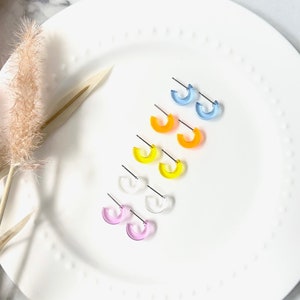 May include: A set of six pairs of colorful acrylic hoop earrings. The earrings are in shades of blue, yellow, orange, pink, and clear.