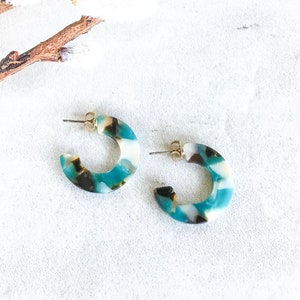 May include: A pair of blue, white, and black hoop earrings. The earrings are made of a marbled plastic material.