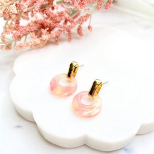 May include: A pair of gold hoop earrings with pink and white marbled accents. The earrings are small and delicate.