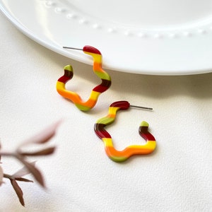 May include: A pair of colorful, wavy hoop earrings. The earrings are made of red, orange, yellow, and green plastic. They are a fun and trendy accessory.