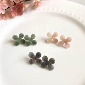 Puede incluir: Tres pares de pendientes con forma de flor. Un par es verde, un par es rosa y un par es gris con vetas blancas.