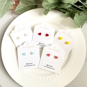 May include: Five cards with the text "BY LUNARI" and a crescent moon logo. Each card features a pair of heart-shaped earrings in different colors: white, red, yellow, light blue, and pink.