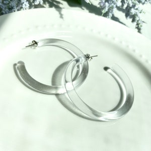 May include: A pair of clear acrylic hoop earrings. The earrings are large and have a simple, modern design.