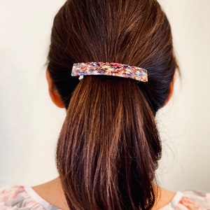 May include: A brown hair ponytail held in place with a colorful, abstract patterned hair clip.