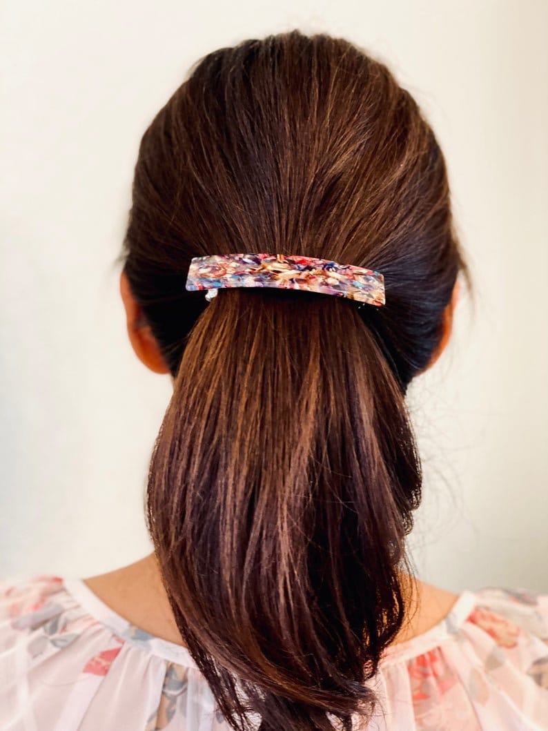 May include: A brown hair ponytail held in place with a colorful, abstract patterned hair clip.