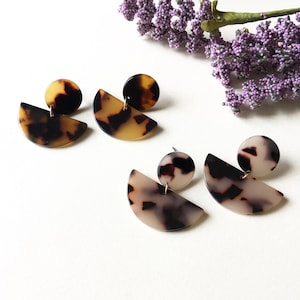 May include: Two pairs of earrings with a geometric design. The earrings are made of brown and white tortoiseshell-patterned resin. The earrings are in the shape of a half-circle with a smaller circle on top.