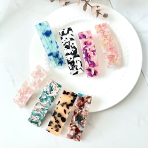 May include: Assortment of eight colorful rectangular hair clips with various patterns, including abstract, animal print, and marbleized designs.