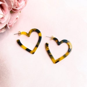 May include: A pair of heart-shaped earrings made of brown and black tortoiseshell-patterned plastic. The earrings have a gold-tone post.