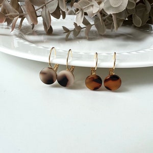 May include: A set of four gold hoop earrings with round, patterned, brown and white resin dangles.