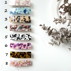 May include: Eight different patterned hair clips in various colors, including pink, blue, brown, black, and white. The clips are arranged vertically on a white background.