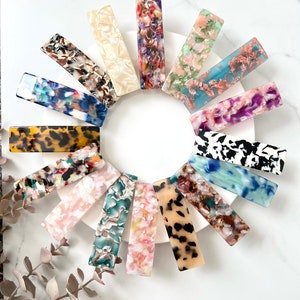 May include: A set of 12 colorful hair clips with a variety of patterns, including tortoise shell, floral, and abstract designs. The clips are made of a durable plastic material and are perfect for holding back hair.