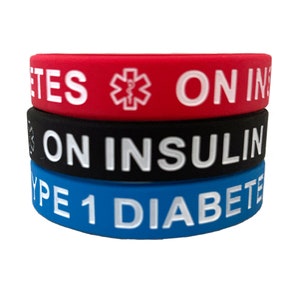 May include: Three silicone wristbands stacked on top of each other. The top band is red with white text that reads "DIABETES ON INSULIN" and a red medical symbol. The middle band is black with white text that reads "ON INSULIN". The bottom band is blue with white text that reads "TYPE 1 DIABETES".