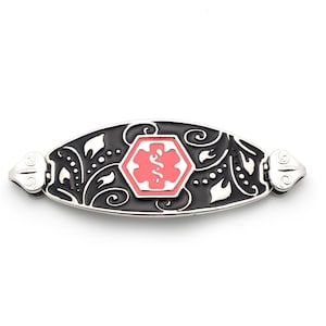 May include: Silver-toned medical alert bracelet with a black background and a red medical symbol. The bracelet has an oval shape with decorative floral and swirl patterns. The medical symbol is a red caduceus inside a red hexagon.