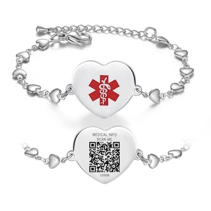 Peut inclure: Un bracelet d'identification médicale argenté avec un pendentif en forme de cœur. Le pendentif présente un symbole médical rouge et un code QR avec le texte "MEDICAL INFO SCAN ME". Le bracelet a une chaîne de petits maillons en forme de cœur.