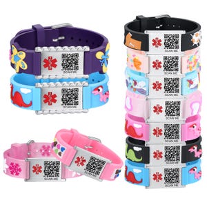 May include: A collection of colorful silicone medical ID bracelets. The bracelets feature various designs, including flowers, dinosaurs, and snowflakes. Each bracelet has a metal plate with a QR code and the text "SCAN ME".