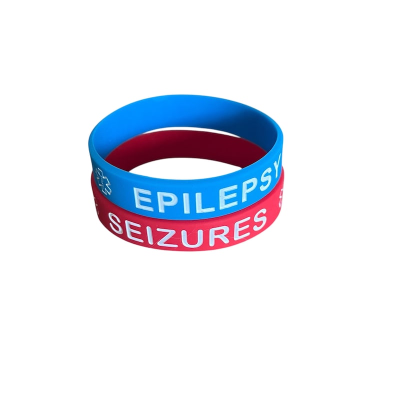 K&ouml;nnte beinhalten: Zwei Silikon-Armb&auml;nder, eines rot und eines blau. Das rote Armband tr&auml;gt die Aufschrift "EPILEPSY SEIZURES" in wei&szlig;en Buchstaben. Das blaue Armband hat ein wei&szlig;es Stern-des-Lebens-Symbol und das Wort "EPILEPSY" in wei&szlig;en Buchstaben.