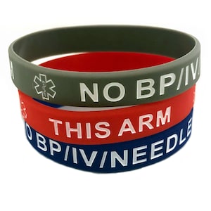 May include: Three stacked silicone wristbands in olive green, red, and navy blue. The olive green band has a medical symbol and the text "NO BP/IV". The red band says "THIS ARM", and the navy band says "NO BP/IV/NEEDLE".