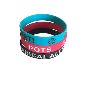 May include: Stack of three medical alert bracelets in teal, red, and black. The teal bracelet has the word "ALERT!" and a medical symbol. The red bracelet says "POTS" and has a medical symbol. The black bracelet says "MEDICAL ALERT".