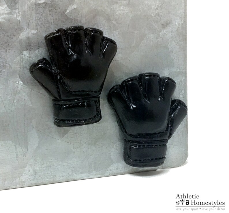 Puede incluir: Dos guantes negros sin dedos de goma con una superficie texturizada. Los guantes est&aacute;n unidos a una superficie met&aacute;lica.