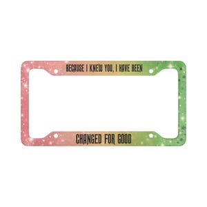 May include: License plate frame with a gradient of pink, orange, and green, speckled with white stars. The frame has the text "BECAUSE I KNEW YOU, I HAVE BEEN" at the top and "CHANGED FOR GOOD" at the bottom in black font.