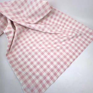 May include: A pink and white gingham fabric, folded and draped, against a white background. The fabric is a classic checkered pattern, with a soft, slightly wrinkled appearance. The color scheme is a light pink and white.