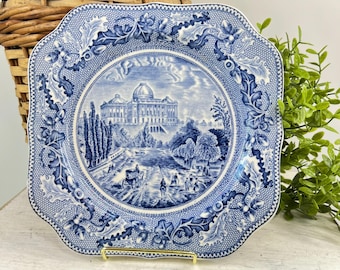 May include: A square ceramic plate featuring a blue and white transferware pattern. The center depicts a large domed building with trees and figures, while the border displays a detailed motif of oak leaves and acorns on a fine mesh background.