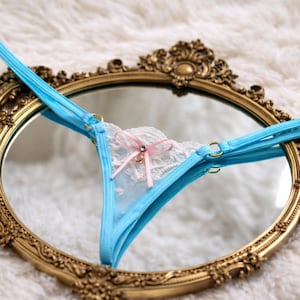 Micro tanga de encaje transparente blanco con tirantes turquesas