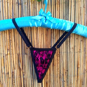 Op de afbeelding: Zwarte kanten lingerie met een roze bloemenpatroon. De lingerie hangt aan een blauwe satijnen hanger.