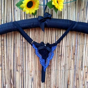 Può includere: Lingerie in pizzo nero con bordino blu e un fiocco di raso nero. La lingerie è appesa a un appendiabiti imbottito nero.