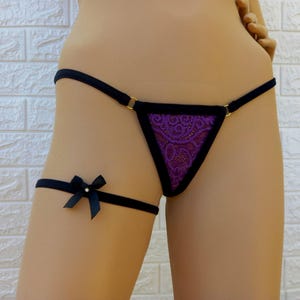 May include: Purple lace lingerie with black trim and a black garter with a bow.