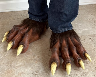 May include: A pair of brown creature feet covers with dark brown fur, textured skin, and long, pointed, off-white claws. The covers are worn over dark blue denim jeans, extending over the top of the feet with a thick layer of fur at the ankles.