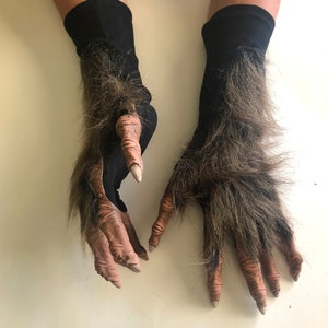 May include: A pair of black and brown werewolf costume gloves with furry details. The gloves have long, clawed fingers.