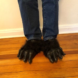 Peut inclure: Une paire de pantoufles de pieds de gorille noires portées sur un jean bleu.