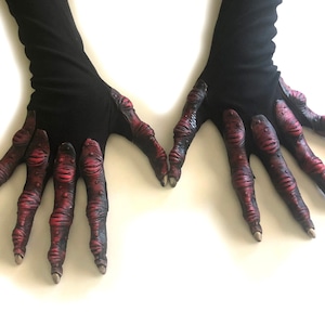 May include: A pair of black gloves with red, clawed hands. The gloves are long and extend past the wrist.