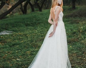 May include: A bride wearing a white lace wedding dress with a long train, standing in a grassy field. She is wearing a beaded face mask and a tiara.