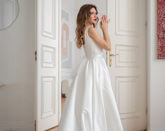 May include: A woman in a white sleeveless wedding dress with a long train stands in a doorway. The dress has a fitted bodice and a flowing skirt.